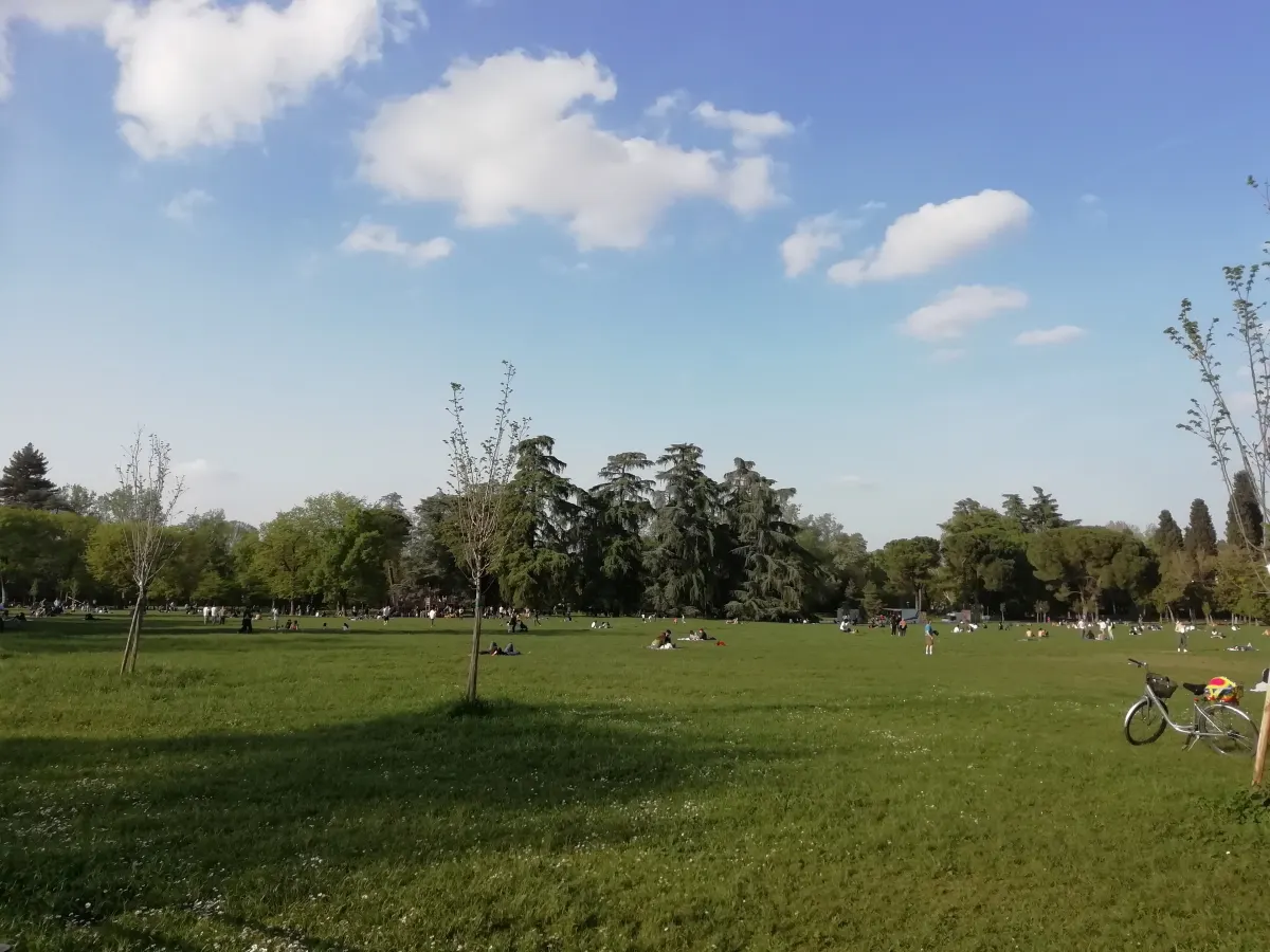 Grande pelouse des Giardini Margherita sous un ciel bleu, promeneurs et vélos