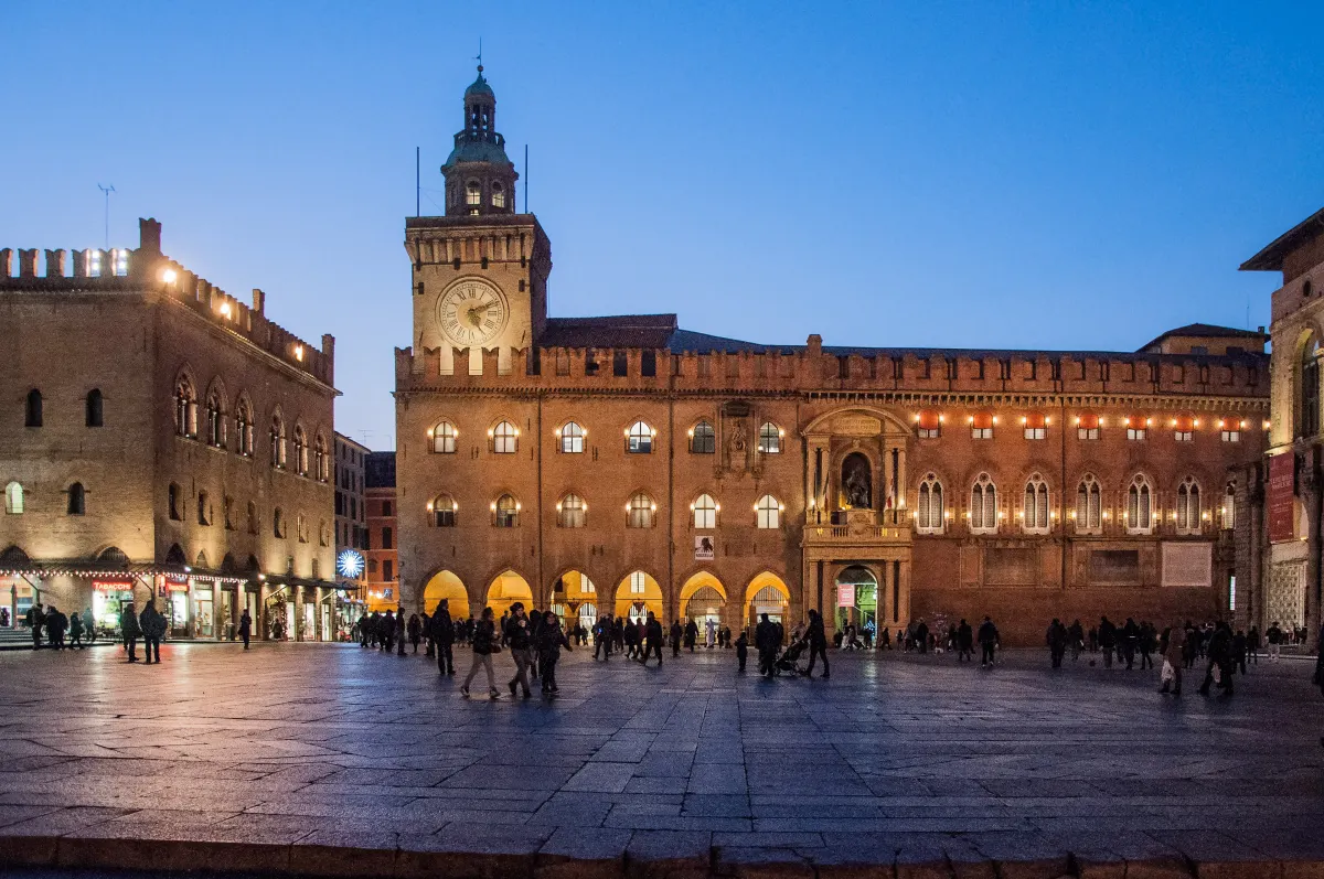 Façade du Palazzo d’Accursio et sa tour de l’Horloge illuminées à la tombée de la nuit, sur la Piazza Maggiore