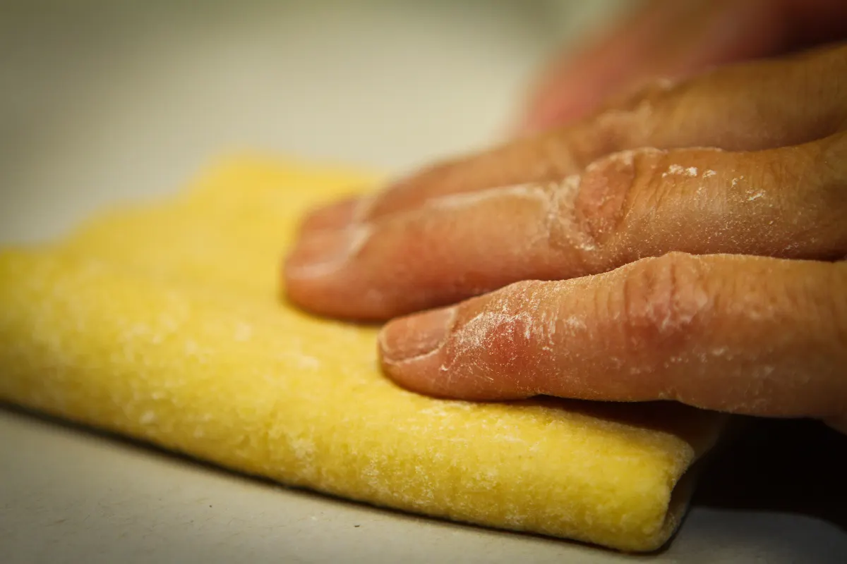 Mains pressant une feuille de pâte fraîche aux œufs sur un plan de travail fariné