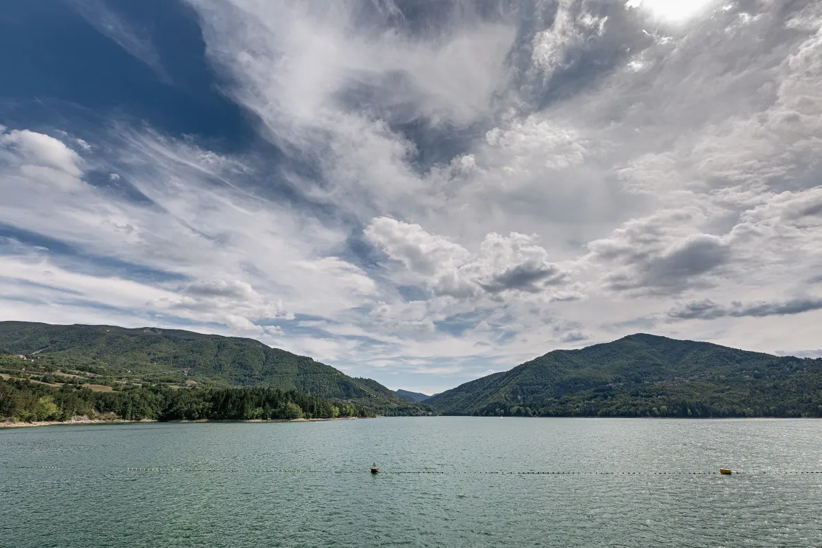 Lac de Suviana entouré de collines boisées sous un ciel nuageux